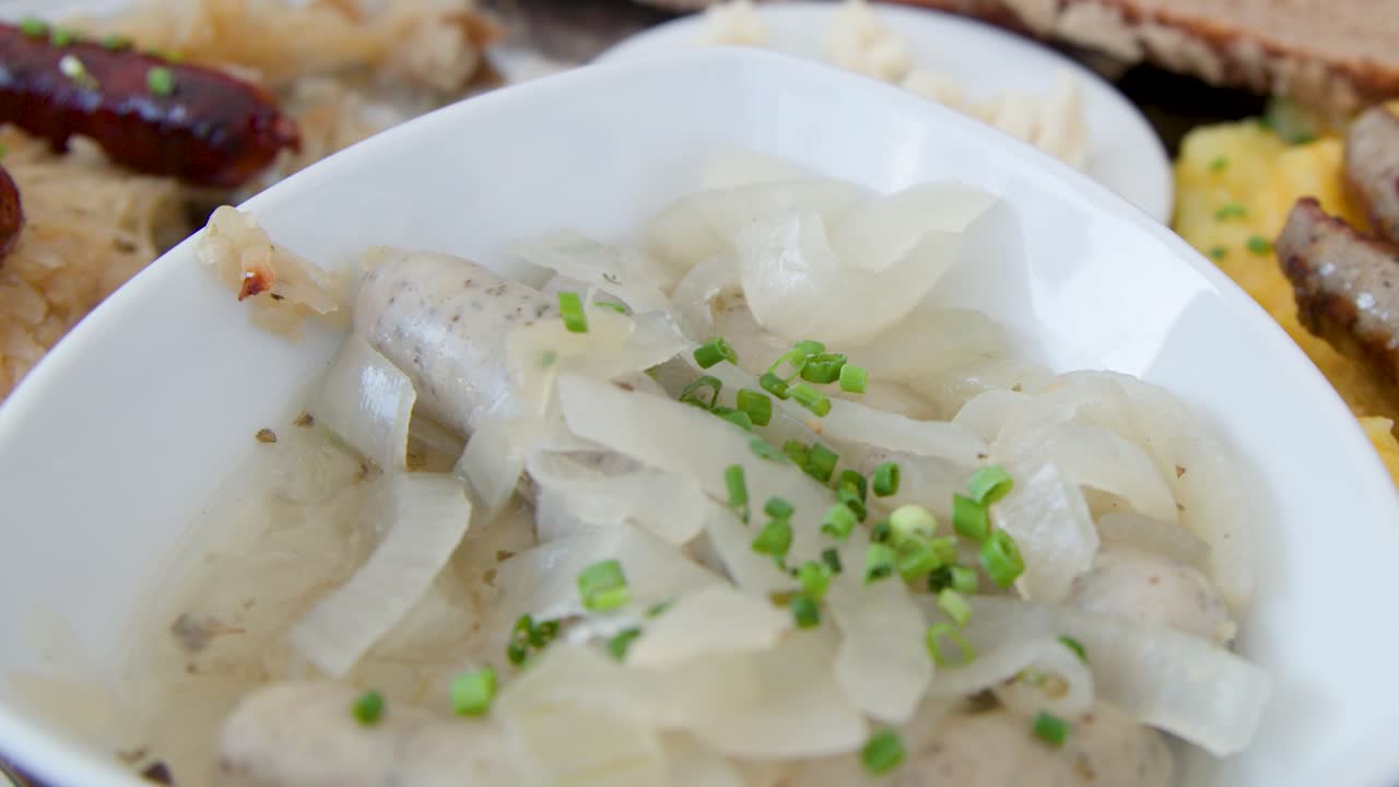 Close-up of fork picking up Nuremberg sausage with onions, bread, sauerkraut, and potato salad