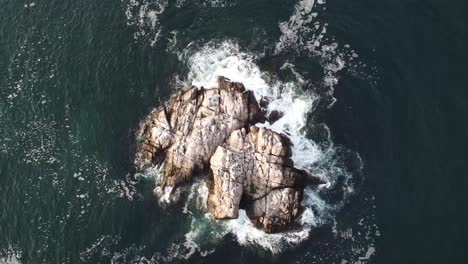 Above-view-of-a-rock-formation-with-ocean-waves-hitting-and-splashing-sea-stack-in-Singing-Beach,-USA