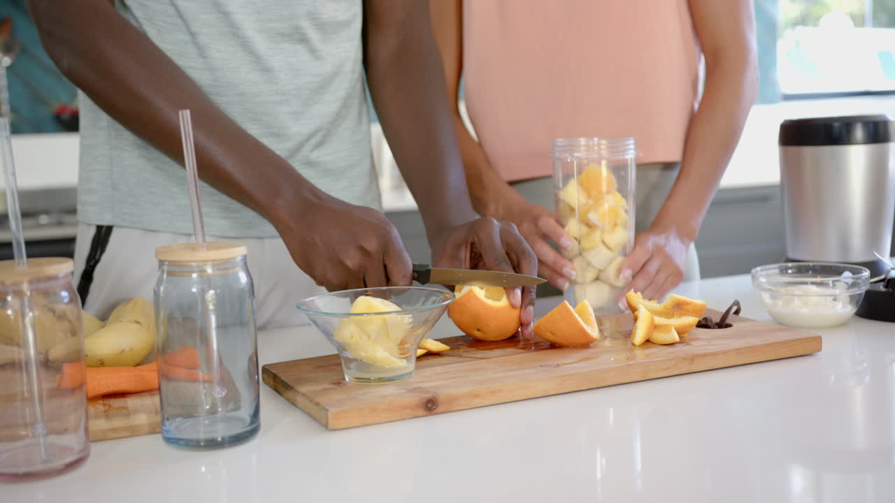 Diverse couple preparing fruit in kitchen, slicing oranges, at home