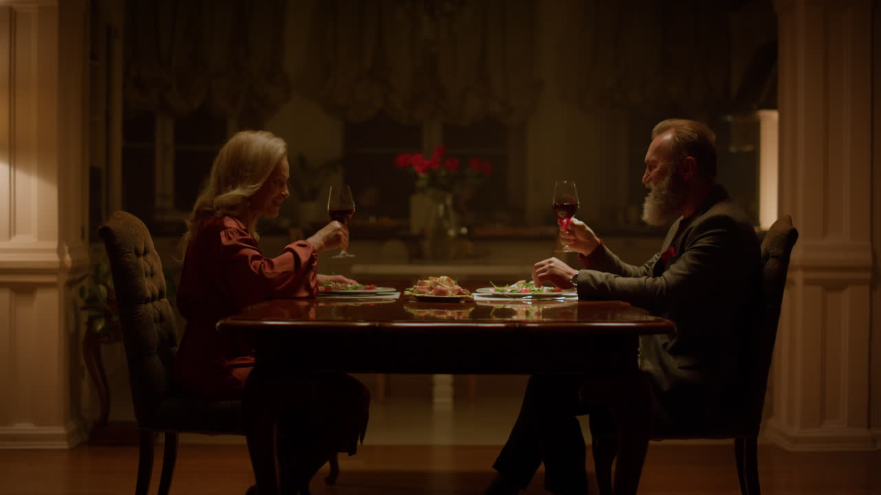 Love old couple clinking glasses wine and making toast at home table. Retirement