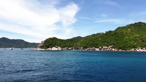 View-from-a-boat-driving-around-a-corner,-revealing-the-small-harbor-of-the-island-in-the-background