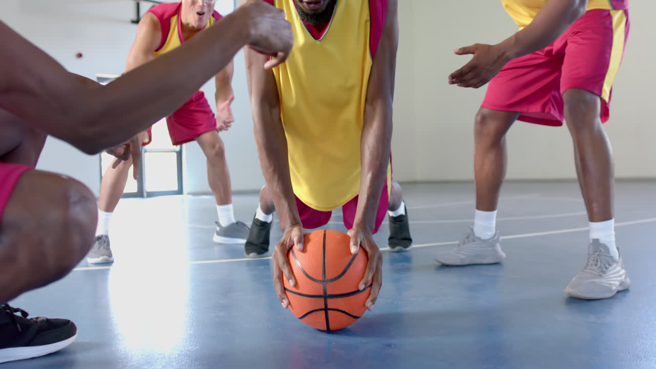 joven afroamericano haciendo flexiones en una pelota de baloncesto en una cancha cubierta