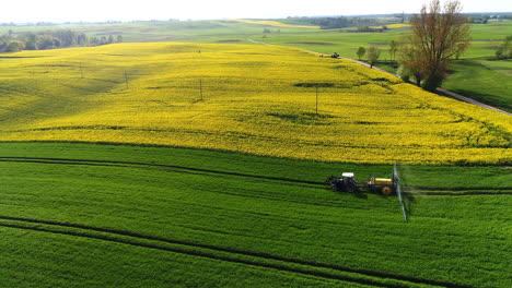 Traktor-Mit-Anhänger-Und-Breitem-Metallarm-Mit-Düsen,-Die-Pestizide-über-Das-Grüne-Feld-Mit-Gelbem-Rapsfeld-Im-Hintergrund-Sprühen