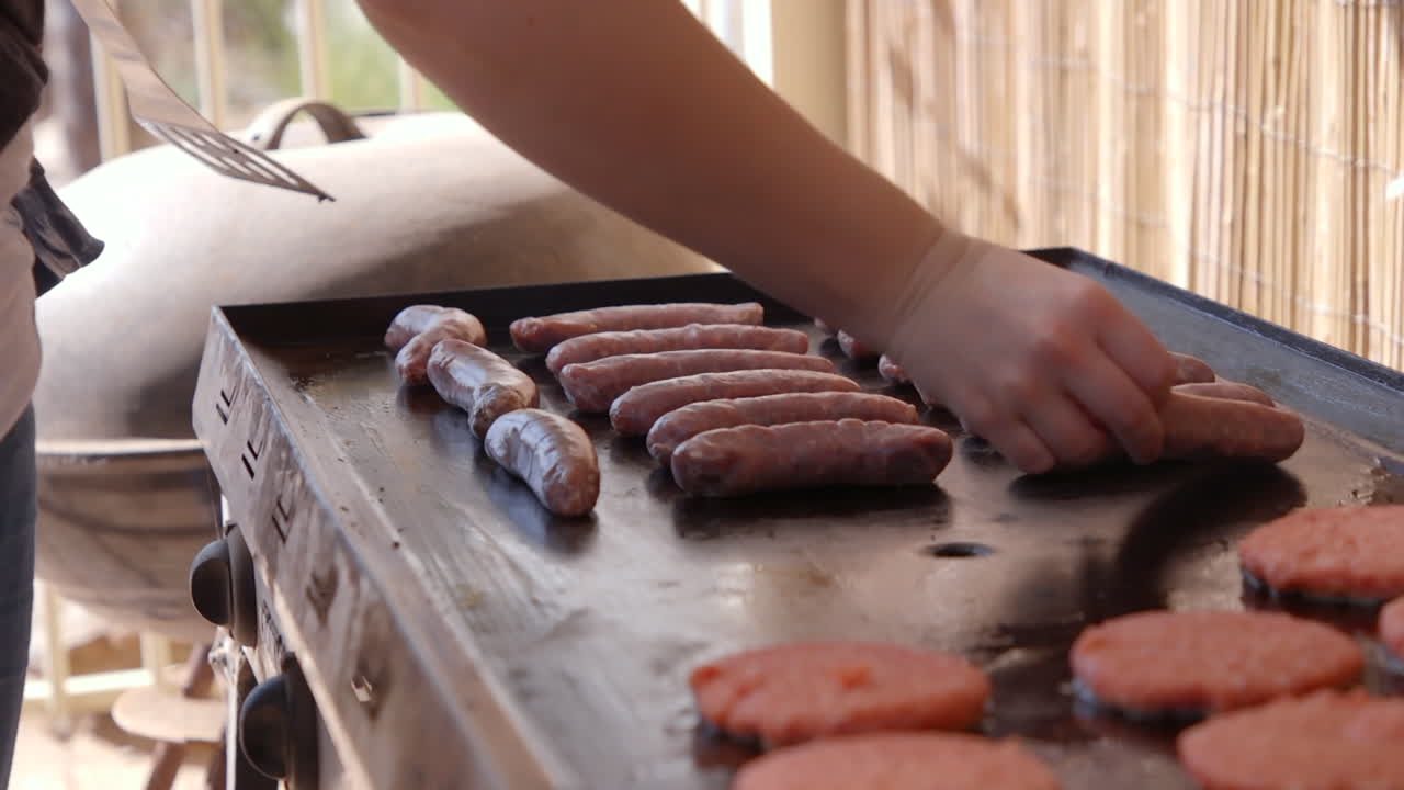 Cooking meat on a barbecue hotplate outside with sausages and hamburgers on a warm sunny day for lunch and dinner