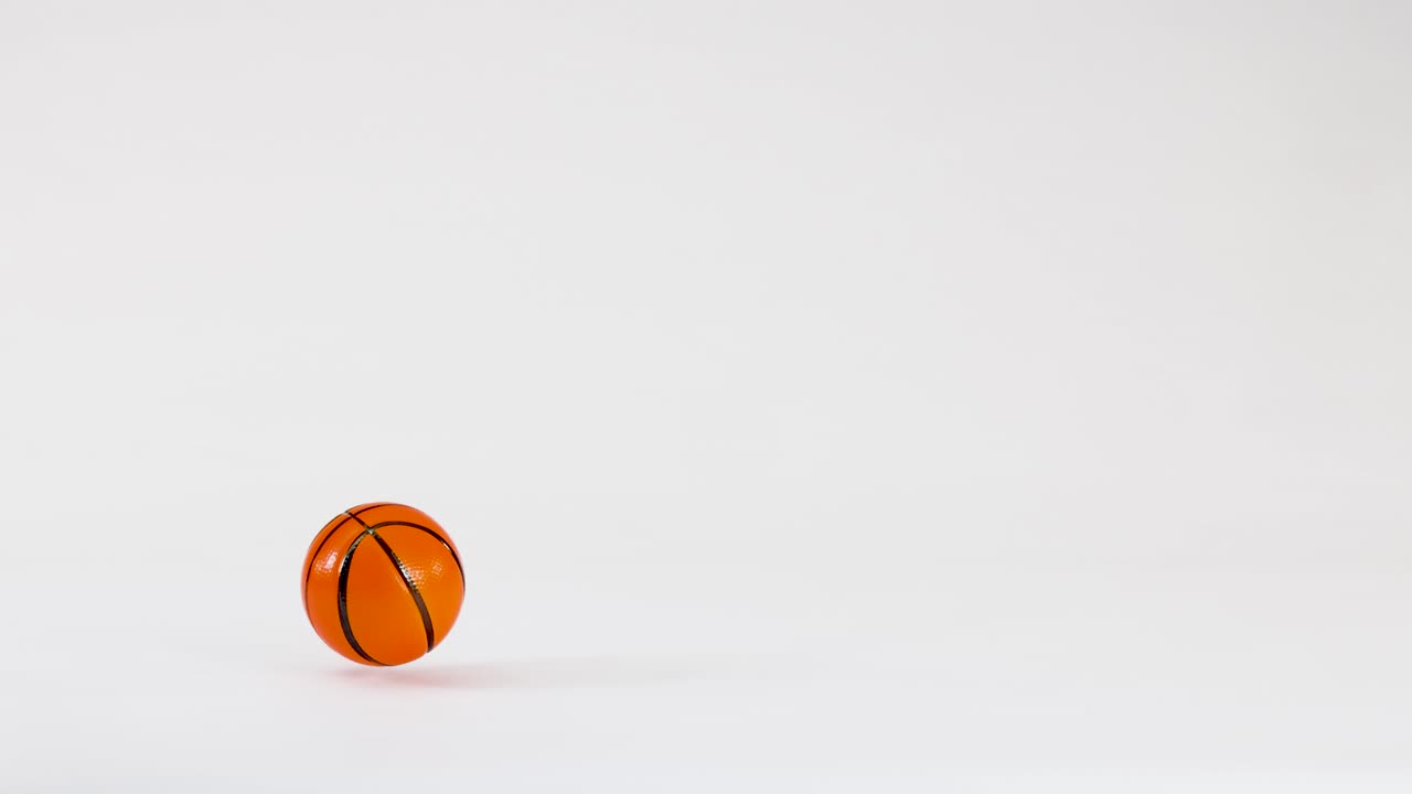 A miniature orange basketball bounces and rolls across a clean white surface with bright lighting