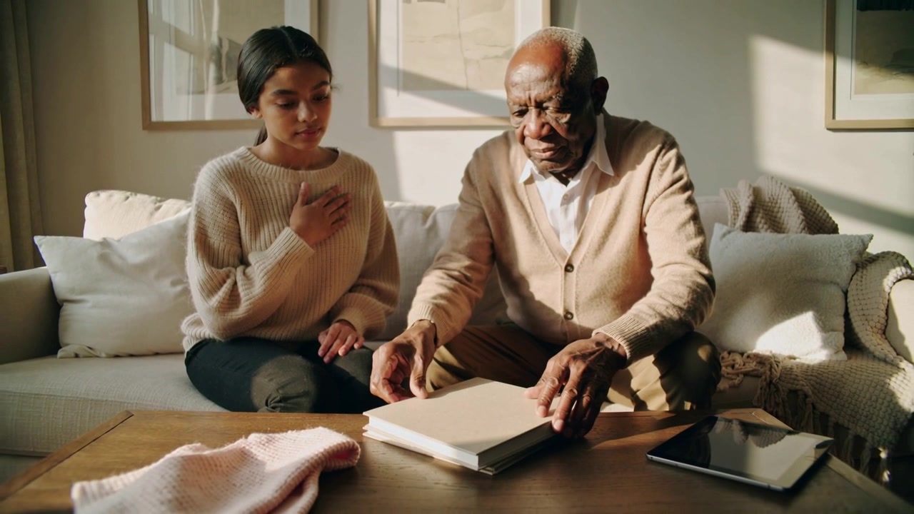 Turning pages grandfather in cardigan handling album at home after grandchild placing hand on chest