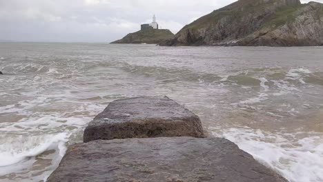 Leuchtturm-Im-Hintergrund,-Während-Wellen-An-Einem-Windigen-Tag-In-Swansea-UK-4k-Auf-Einen-Erodierten-Steg-Krachen