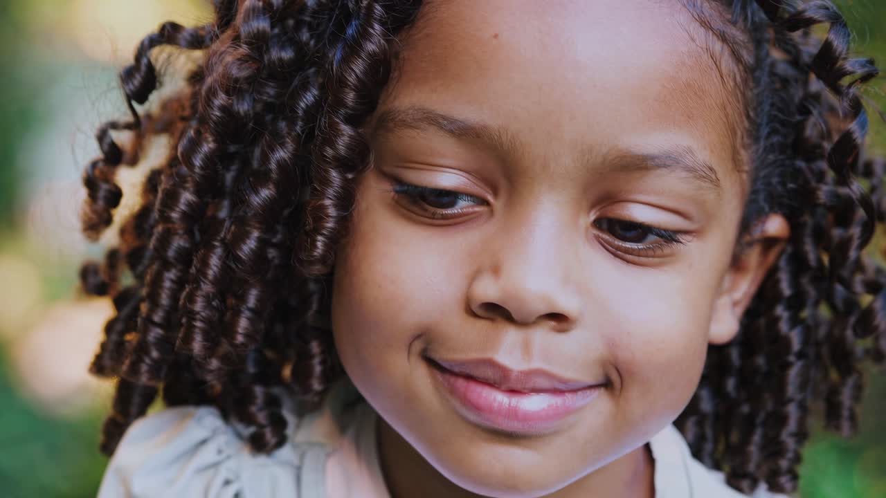 Close-up video still of a smiling child with curly hair, captured at eye level