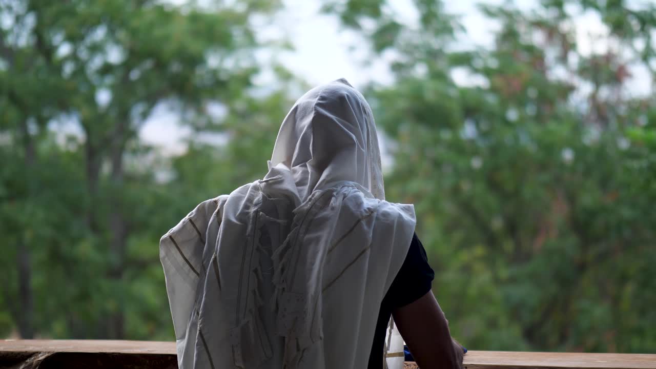 Hombre rezando con talit, meciéndose suavemente mientras sostiene un libro de oraciones