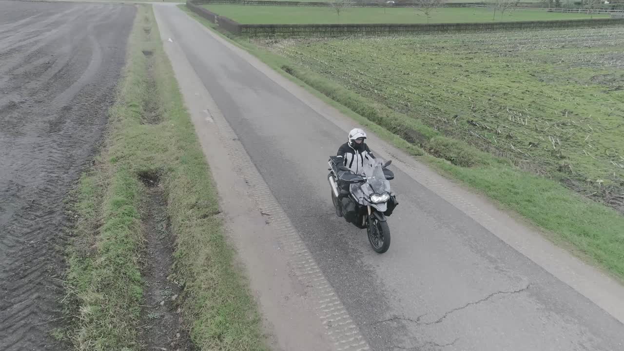 Drone shot of motorcyclist driving down farm fields