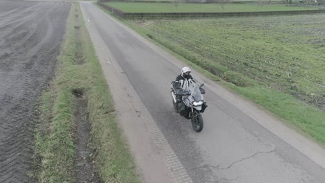 drone shot of motorcyclist driving down farm fields