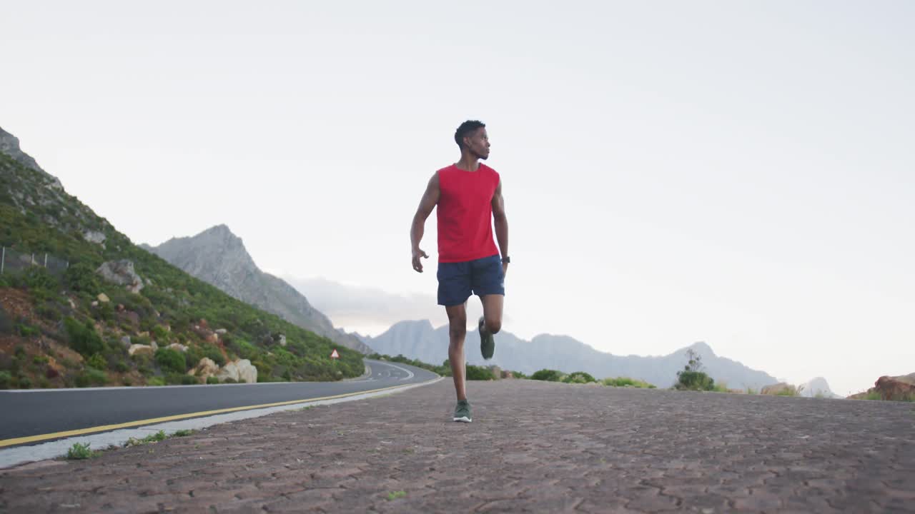 hombre afroamericano actuando estirando las piernas mientras está de pie en la carretera