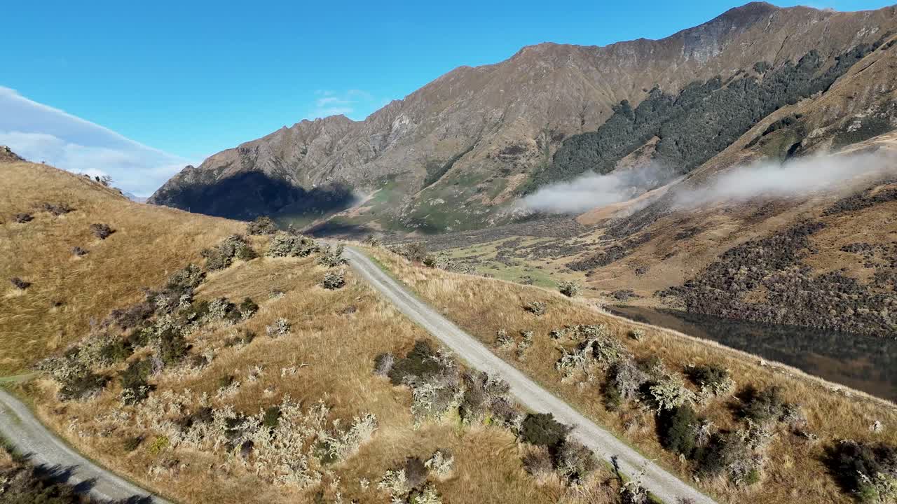 Aerial view of a winding road through mountainous terrain, revealing a serene lake under clear blue skies