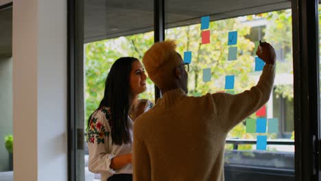 Young-mixed-race-business-colleagues-discussing-over-sticky-notes-in-modern-office-4k