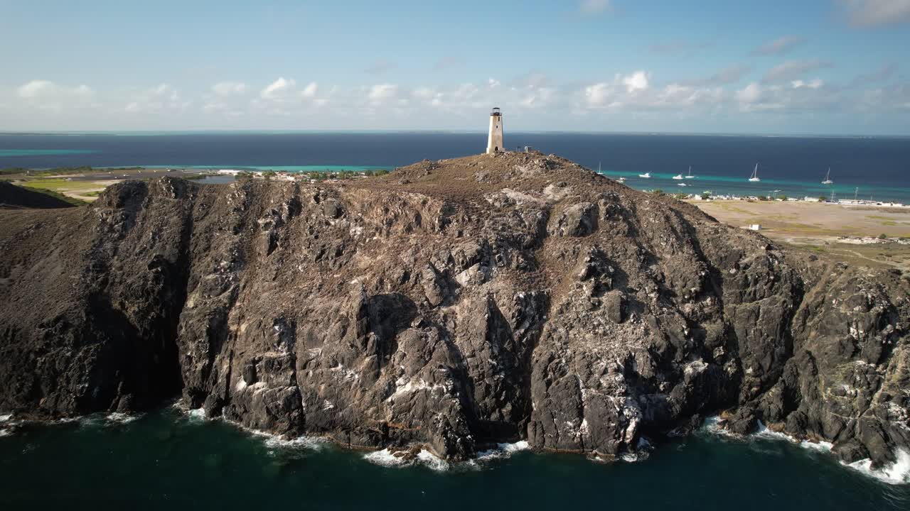 바위 절벽 위에 있는 등대, 배경에는 바다와 먼 마을이 있습니다.