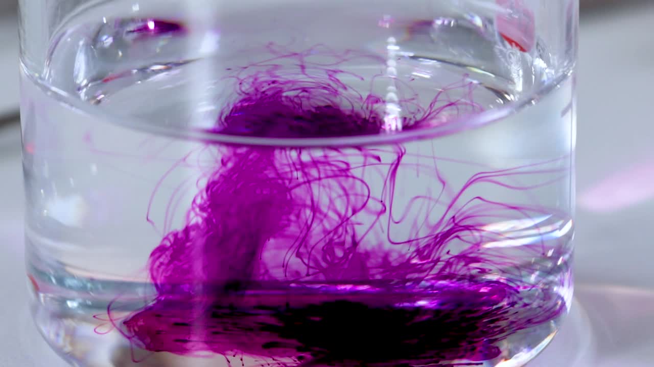 Observe the striking diffusion of purple color in a clear liquid within a glass container.
