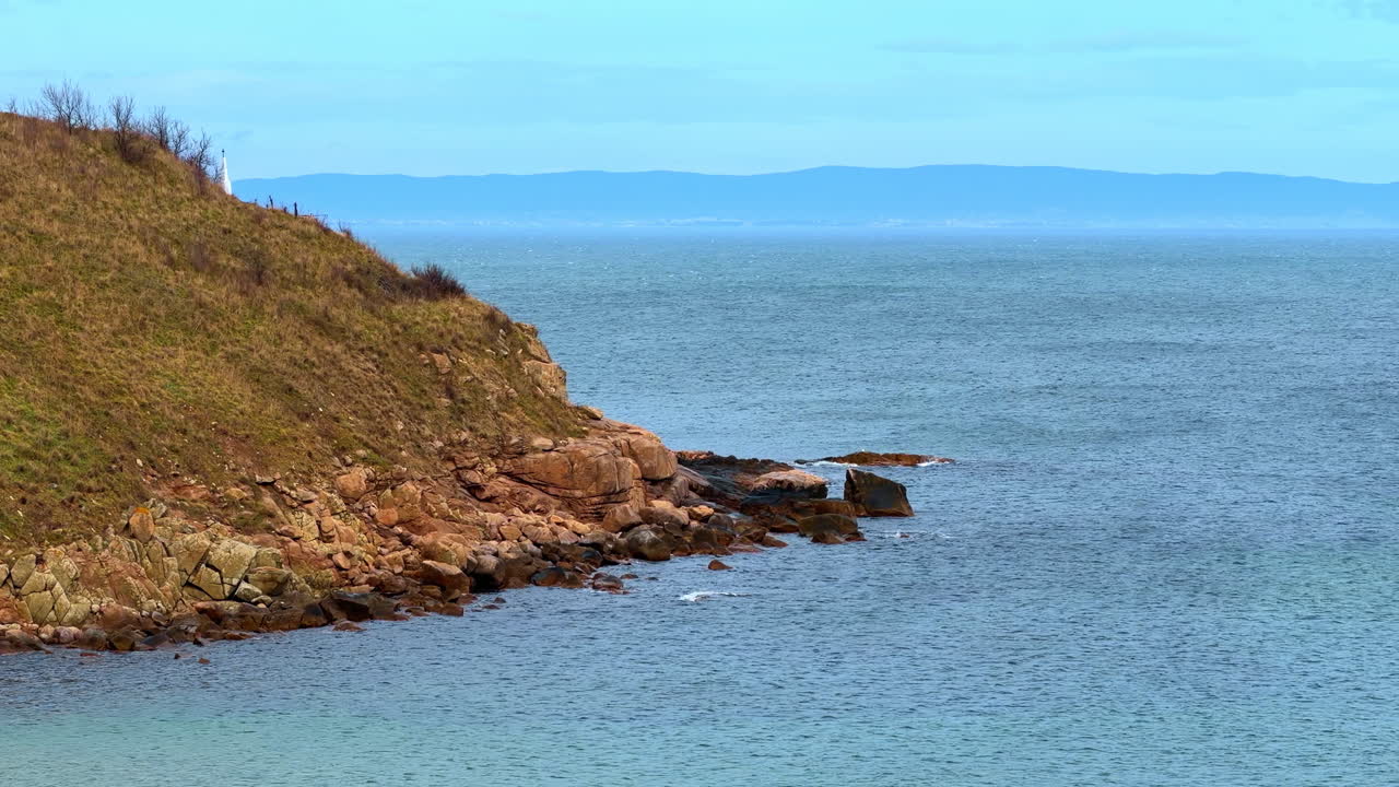 Vista della costa con rocce e acqua blu vicino alla terra con tempo sereno. La scena mostra una costa rocciosa con acqua blu che si estende in lontananza.