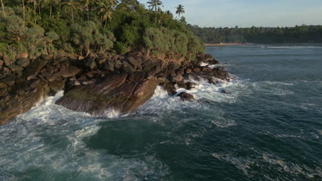 establishing aerial drone shot of waves crashing against rocks 60 fps with bay in background in sri lanka south coast