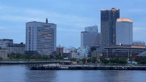 Twilight-cityscape-with-waterfront,-modern-buildings-reflecting-sunset-light,-tranquil-urban-scene