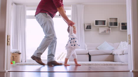 Padre-Ayudando-A-Su-Hija-A-Aprender-A-Caminar-En-Casa,-Vista-Lateral