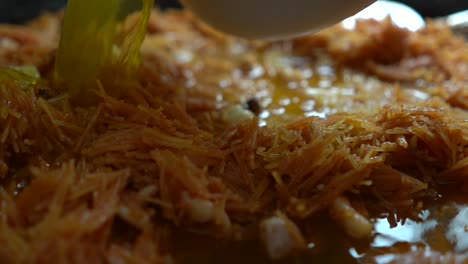 adding the broth for mediterranean fideua to paellon with ingredients and noodles