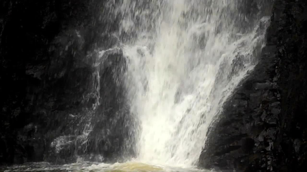 un primer plano de una cascada que desemboca en una piscina seguida de una lenta inclinación hacia arriba