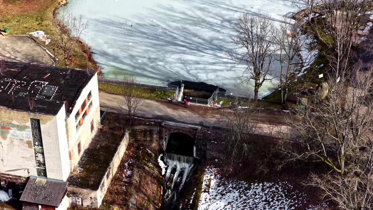 Frozen lake surface with tree shadows and an old industrial building
