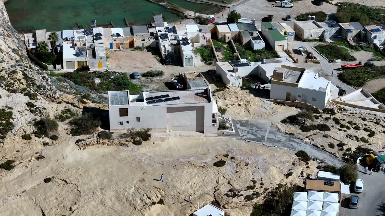 Una perspectiva aérea captura la tranquila historia de un pueblo costero enclavado contra los acantilados de piedra caliza en Dwejra Gozo Malta durante un brillante día de verano con condiciones climáticas soleadas y despejadas.