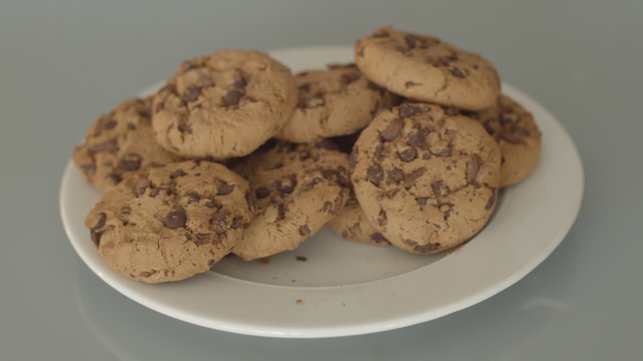 Hand taking chocolate chip cookies from a white plate - high angle
