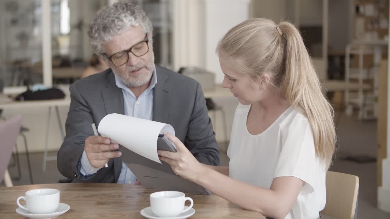 Bearded Caucasian executive manager holding clipboard while blond client signs documents