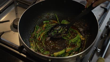 pak choi and chilli paste being stirred in oil inside wok