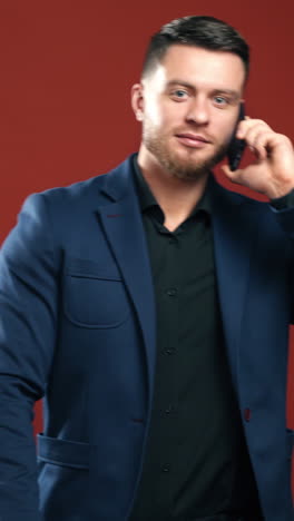 happy businessman talking the phone. handsome man in suit holding folder and speaking on the phone in studio. office manager on dark red background. vertical video