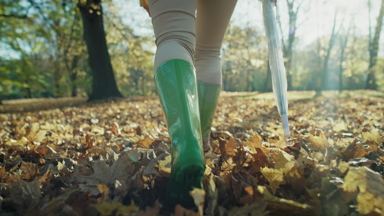 Low section of woman's legs wearing rain boots walking in forest with umbrella.