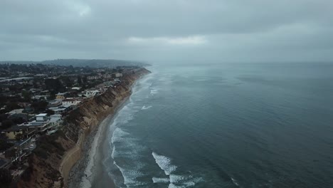 Blick-Von-Einer-Drohne,-Die-über-Den-Ozean-Aufsteigt-Und-Das-Meer,-Den-Strand-Und-Eine-Stadt-Nahe-Dem-Rand-Einer-Klippe-Zeigt