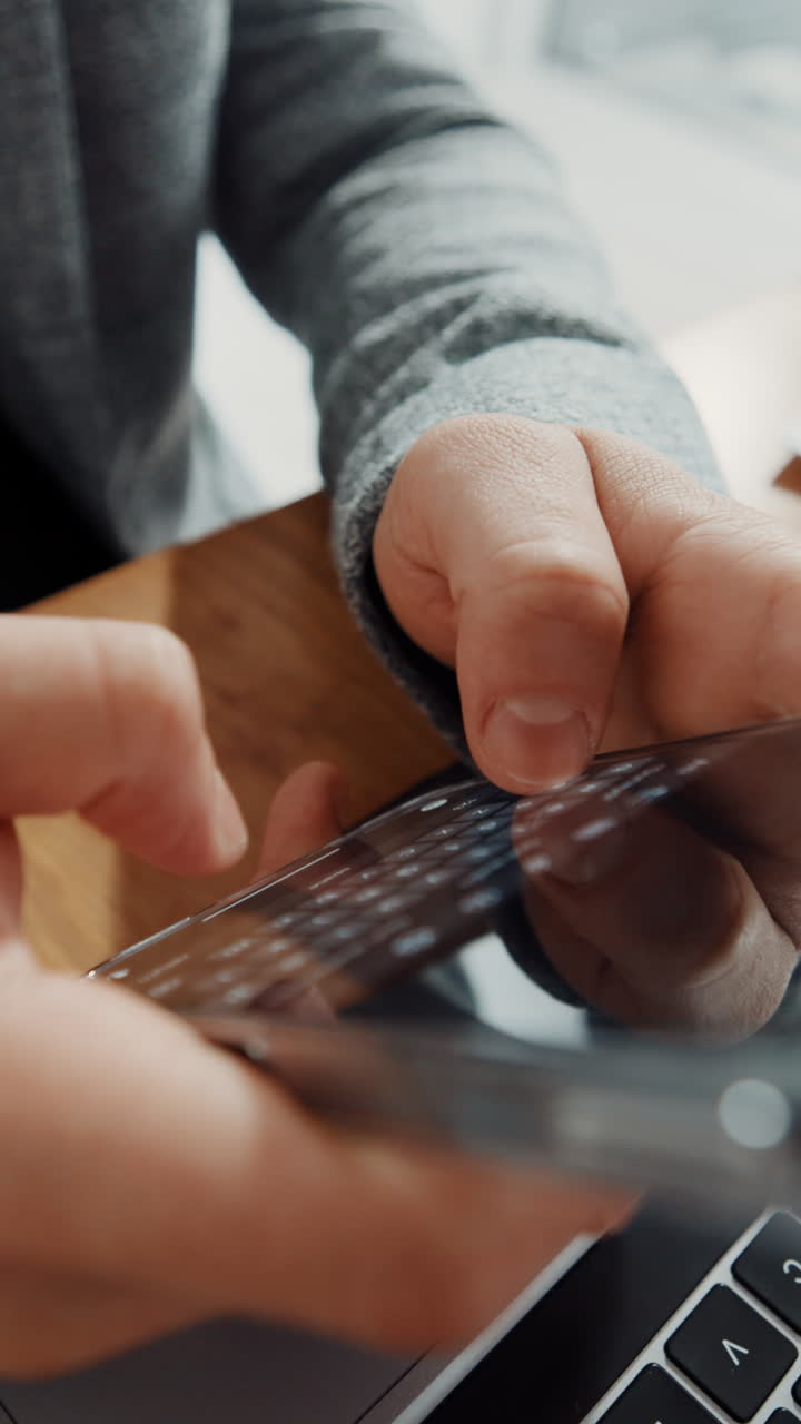 Close-up of Hands Typing on Smartphone Screen with Laptop