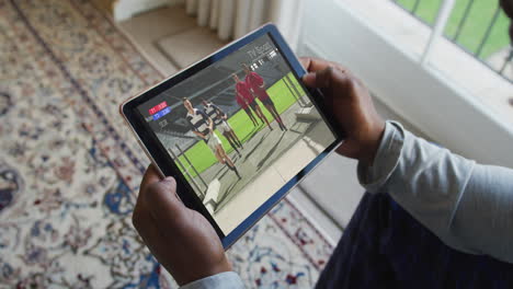 compuesto de un hombre sentado en casa viendo un partido de rugby en una tableta