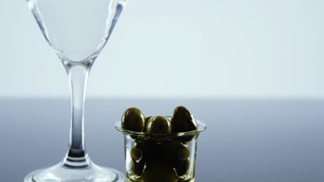 glass of cocktail and green olives in a glass cup