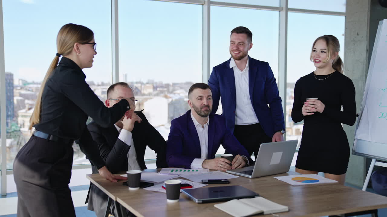 Collaborating team of men and women in the office. Friendly people co working and discussing ideas. City scenery at the background.