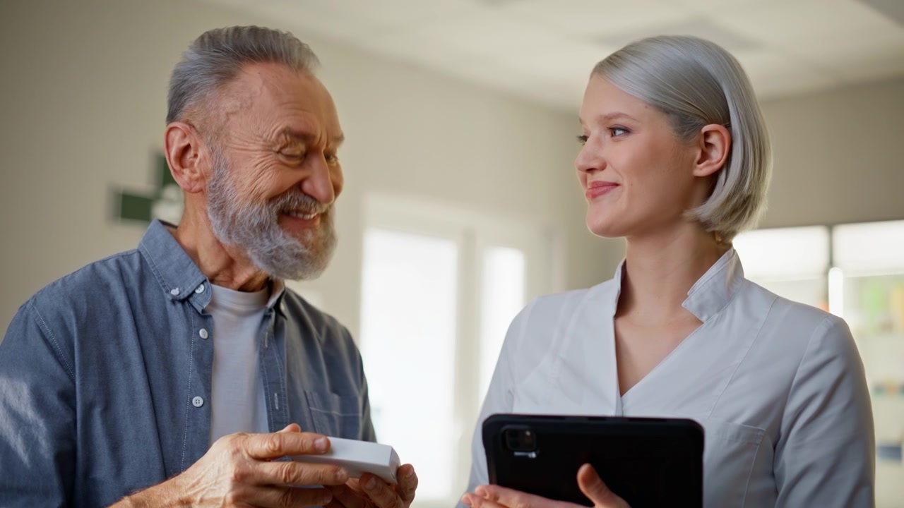 Mani del medico che digitano su un tablet scegliendo una medicina per un cliente anziano, primo piano all'interno.