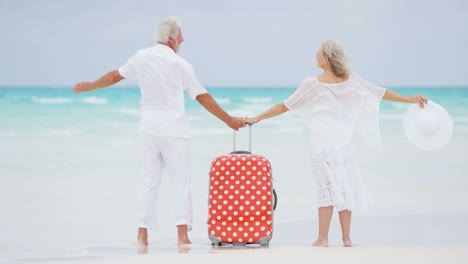 barefoot mature caucasian couple on beach with suitcase