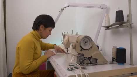 Professional-tailor-working-on-sewing-machine-in-studio-workshop,-Profile