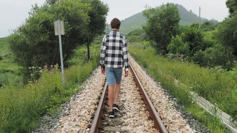 teenage boy walking on train tracks in nature