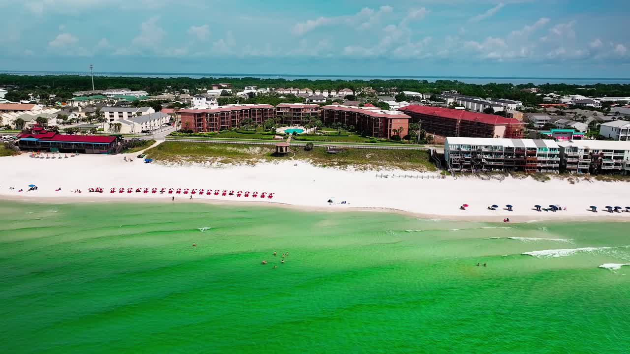 destino del avión no tripulado volando lateralmente sobre el golfo de méxico con una vista de la arena blanca, agua verde esmeralda, restaurante pompano joe, carrito de golf, estacionamiento, sillas de playa y paraguas 2 de 2