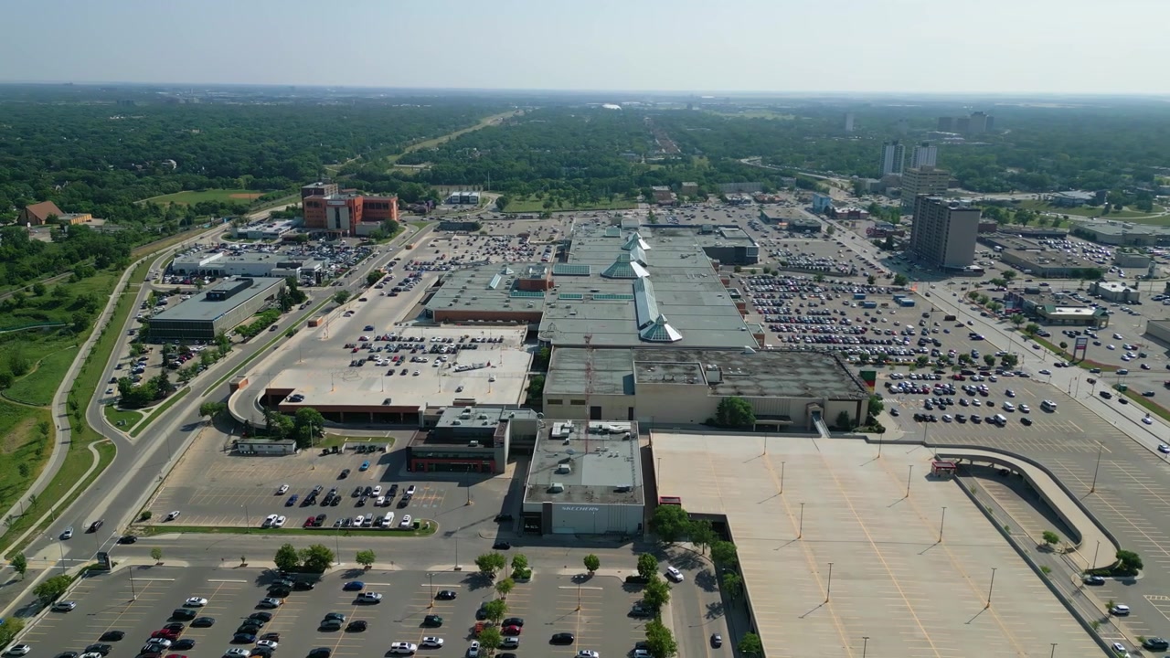 Aerial drone orbit of CF Polo Park showcasing the entire shopping centre, surrounding commercial district, roadways, and parking areas on a bright summer day