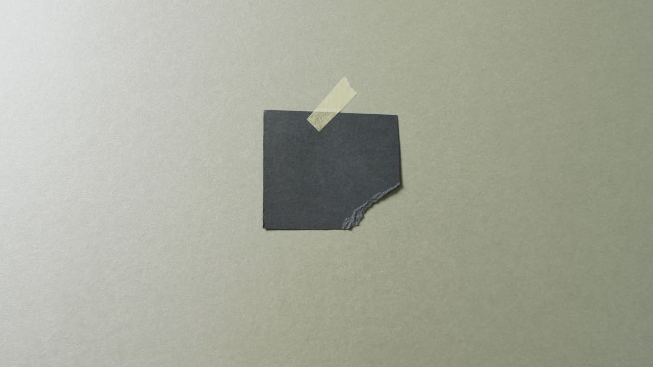 Video of close up of torn piece of black paper taped on green background