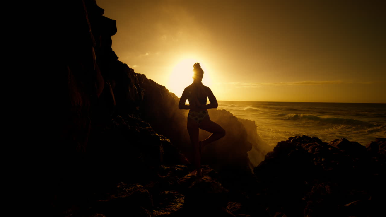 Woman practicing yoga at sunset on a rocky beach