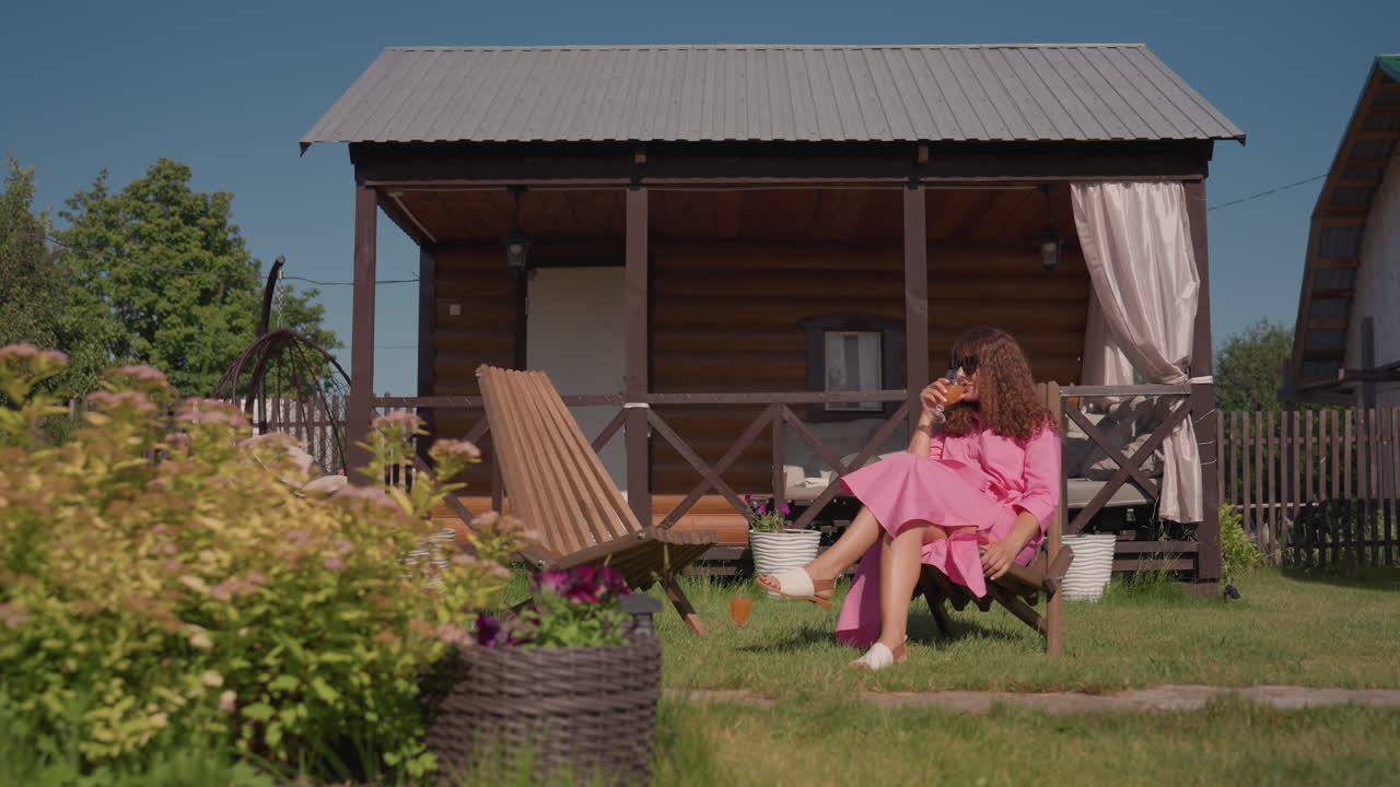 Caucasian Woman Tending Garden Plants, Woman Crouching At Cottage Porch To Tend To Garden Plants And Soil, Caucasian Woman Kneeling By Cottage To Care For Flowers And Soil On Bright Backyard Lawn