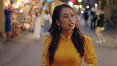 attractive vietnamese woman in traditional dress walks along night street in hoi an in slow motion