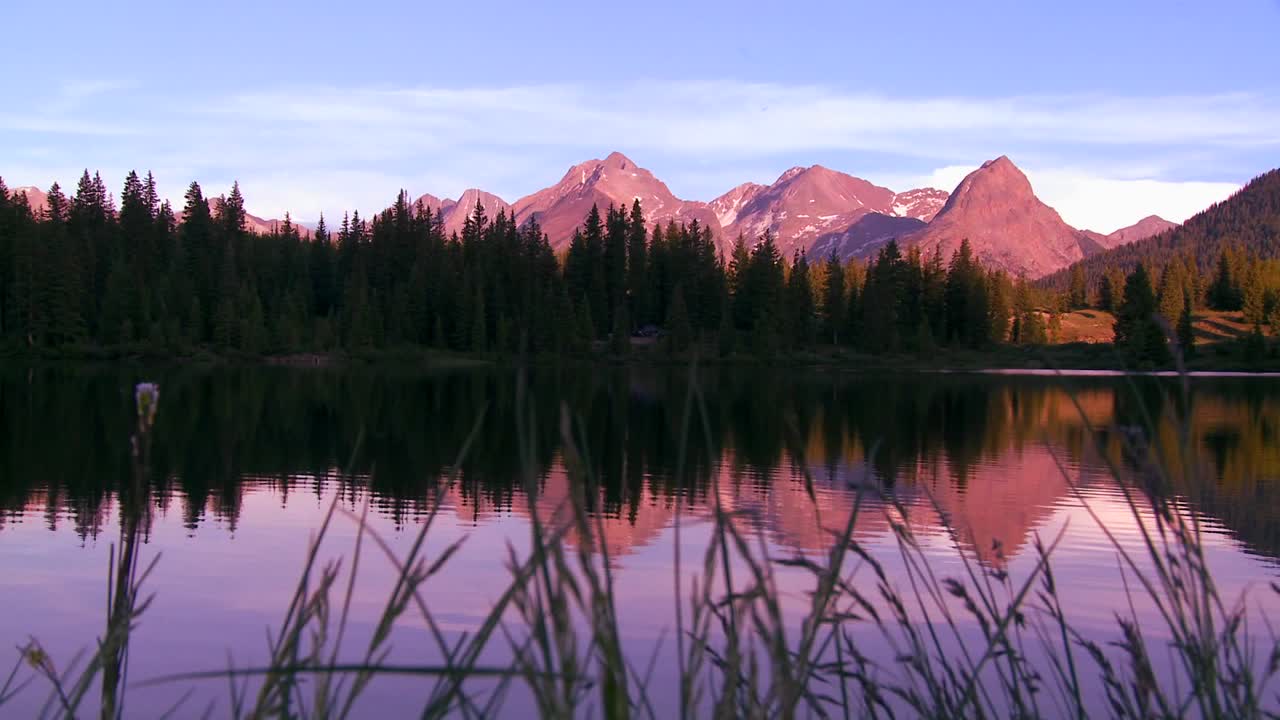 The Rocky Mountains are perfectly reflected in an alpine lake at sunset or dawn in this traveing shot 1