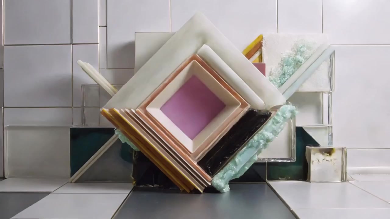 Un quadrato color verde acqua che appare, dando il via a una scultura che ruota e forma una pila compatta in studio, con un cubo color ambra.